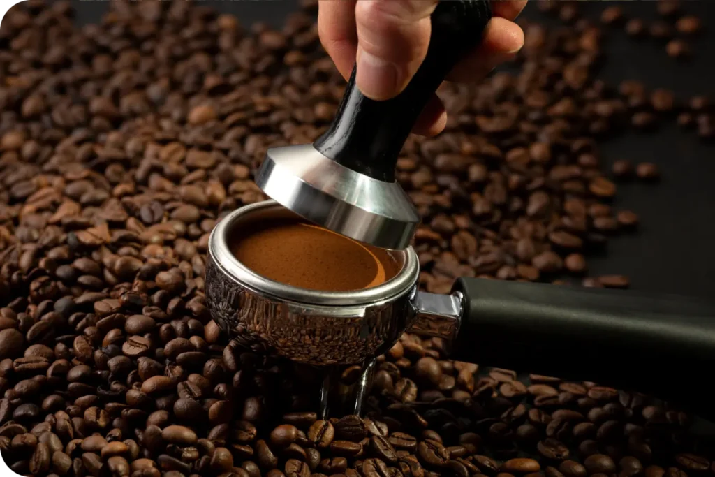 Prensado de café molido en un portafiltro con un tamper sobre granos de café tostados
